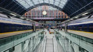 Moderner Bahnhof mit Zügen an den Gleisen und einer großen Bahnhofsuhr im Hintergrund.