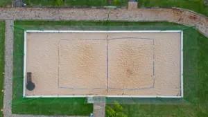 Luftaufnahme eines leeren Beach-Tennis-Platzes mit Sand, umgeben von grünem Rasen.