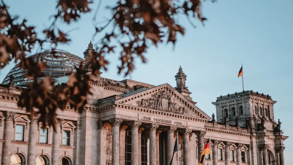 Das Reichstagsgebäude in Berlin unter blauem Himmel mit wehender deutscher Flagge.