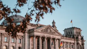Das Reichstagsgebäude in Berlin unter blauem Himmel mit wehender deutscher Flagge.