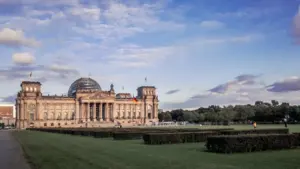 Das Berliner Reichstagsgebäude unter blauem Himmel mit Wiese im Vordergrund.