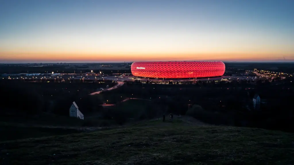 Die beleuchtete Allianz Arena in München bei einem malerischen Sonnenuntergang über der Stadt.
