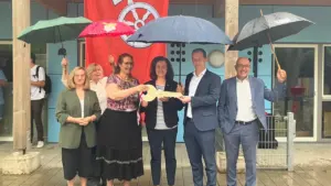Eine Gruppe von Menschen hält bei Regen einen symbolischen großen Schlüssel vor einer Fahne.