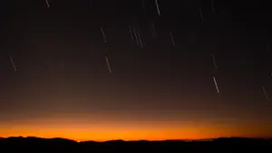 Sternschnuppen am nächtlichen Himmel über einer dunklen Hügellandschaft während der Perseiden-Nacht.