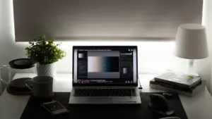Ein aufgeräumter Schreibtisch mit Laptop und Lampe in gemütlicher Abendstimmung.