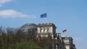 Das Berliner Reichstagsgebäude mit wehenden deutschen und europäischen Flaggen bei Sonnenschein.
