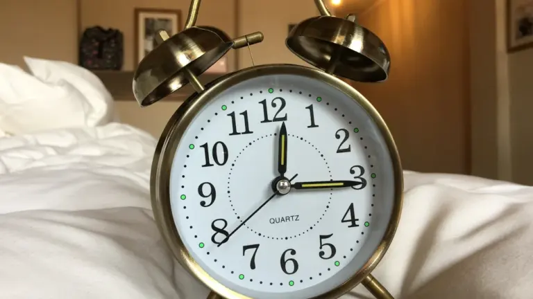 Klassischer Wecker auf weißem Bettlaken symbolisiert den Moment des Aufwachens im Schlafzimmer.