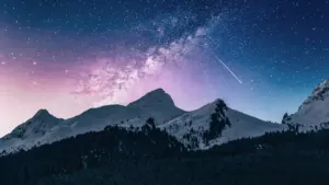 Spektakuläre Sternennacht mit schneebedeckten Berggipfeln und Milchstraße über dem nächtlichen Himmel.