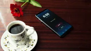 Ein Smartphone und eine Tasse Kaffee auf einem Holztisch am frühen Morgen.