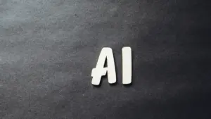 Der Schriftzug KI aus weißen Buchstaben auf einer dunklen, strukturierten Oberfläche.