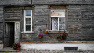 Rustikales altes Holzhaus mit Blumen am Fenster und offenen Türen im Sommer.