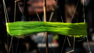 Ein leuchtend grünes Garnknäuel auf einem hölzernen Rahmen für textile Kunst.
