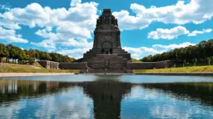 Das Völkerschlachtdenkmal in Leipzig spiegelt sich im Wasserbecken unter blauem Himmel.