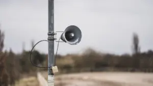 Eine alte Warnsirene auf einem Mast in einer deutschen Stadt bei bewölktem Himmel.
