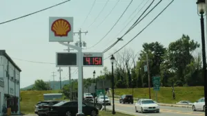 Eine Shell-Tankstelle mit Preisanzeige an einer befahrenen Straße bei Tageslicht.