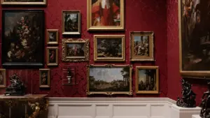 Klassische Gemäldegalerie mit zahlreichen gerahmten Kunstwerken an einer prunkvollen dunkelroten Wand.